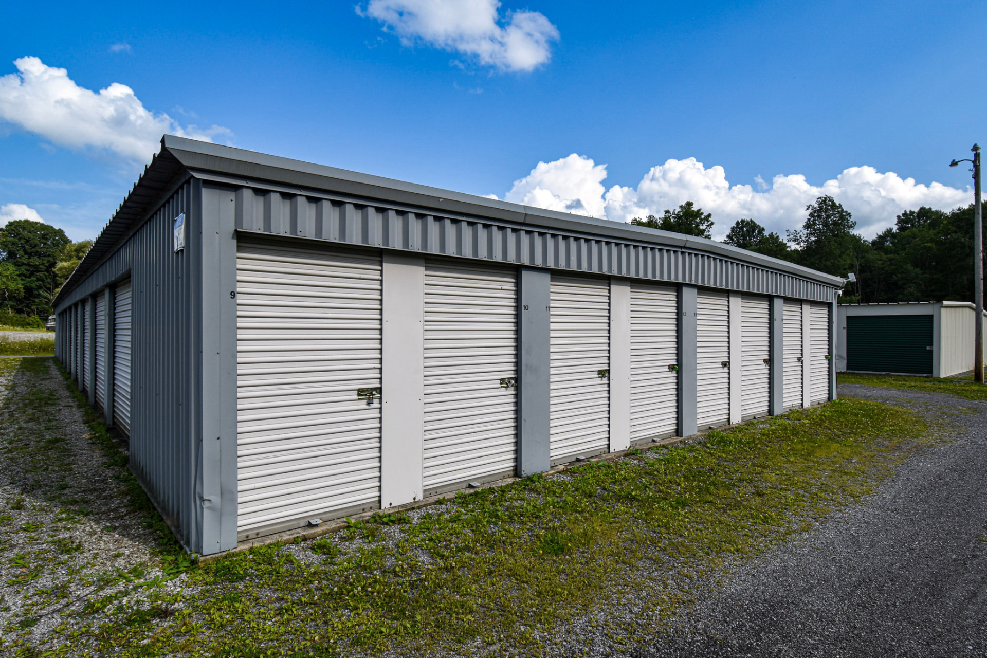 Before: the original storage building with pale doors and vegetation along the gravel drive.