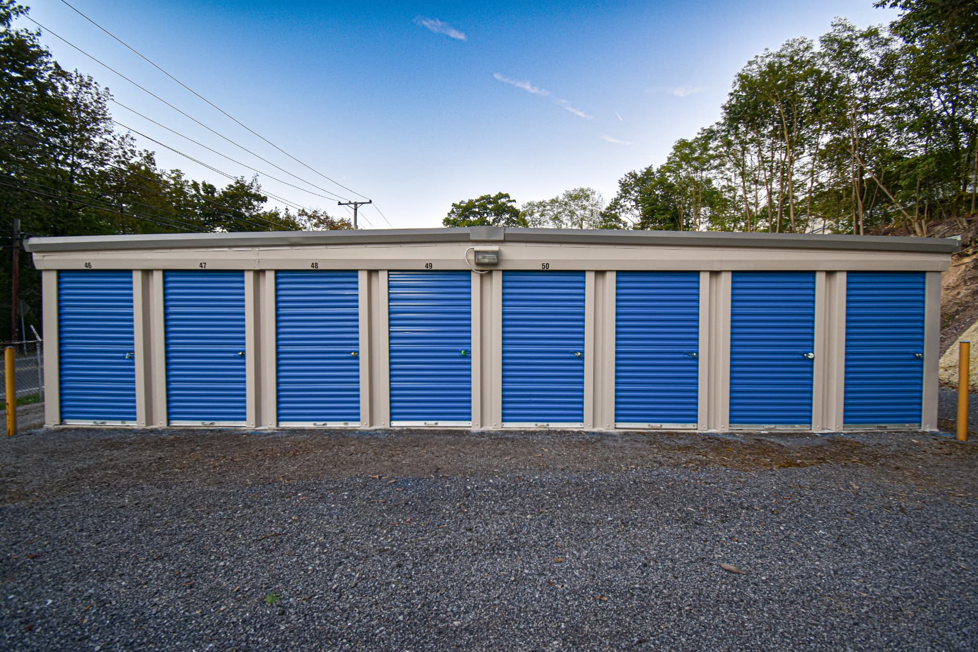 A row of storage units with new blue roll-up doors, clean trim, and fresh gravel.